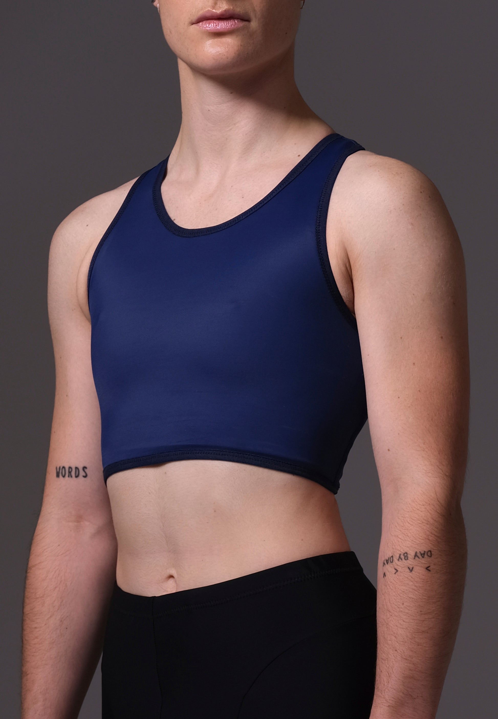 Non-Binary model Chris wearing a navy blue Tank Swim Binder and black shorts on a gray background