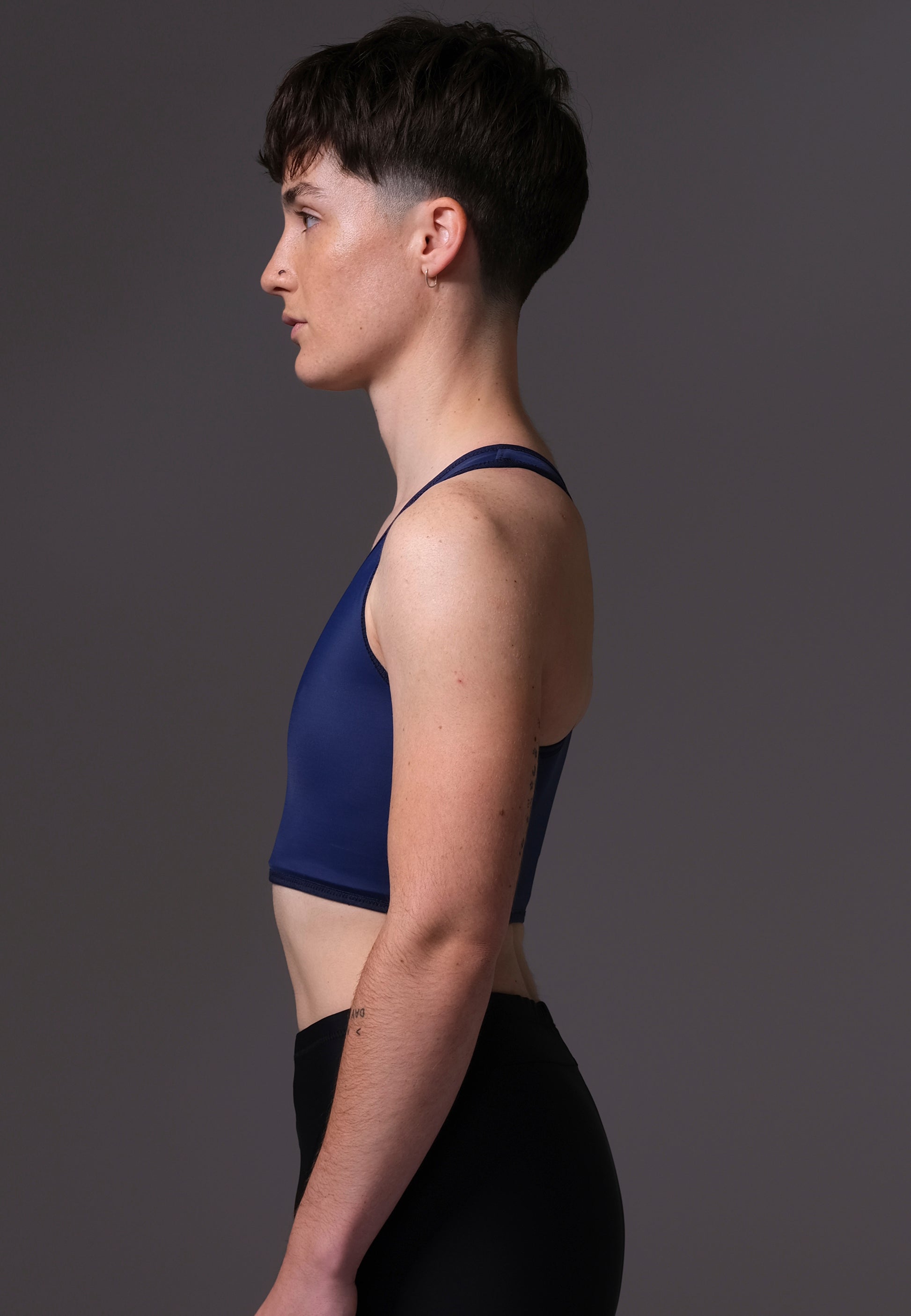 Non-Binary model Chris wearing a navy blue Tank Swim Binder and black shorts on a gray background