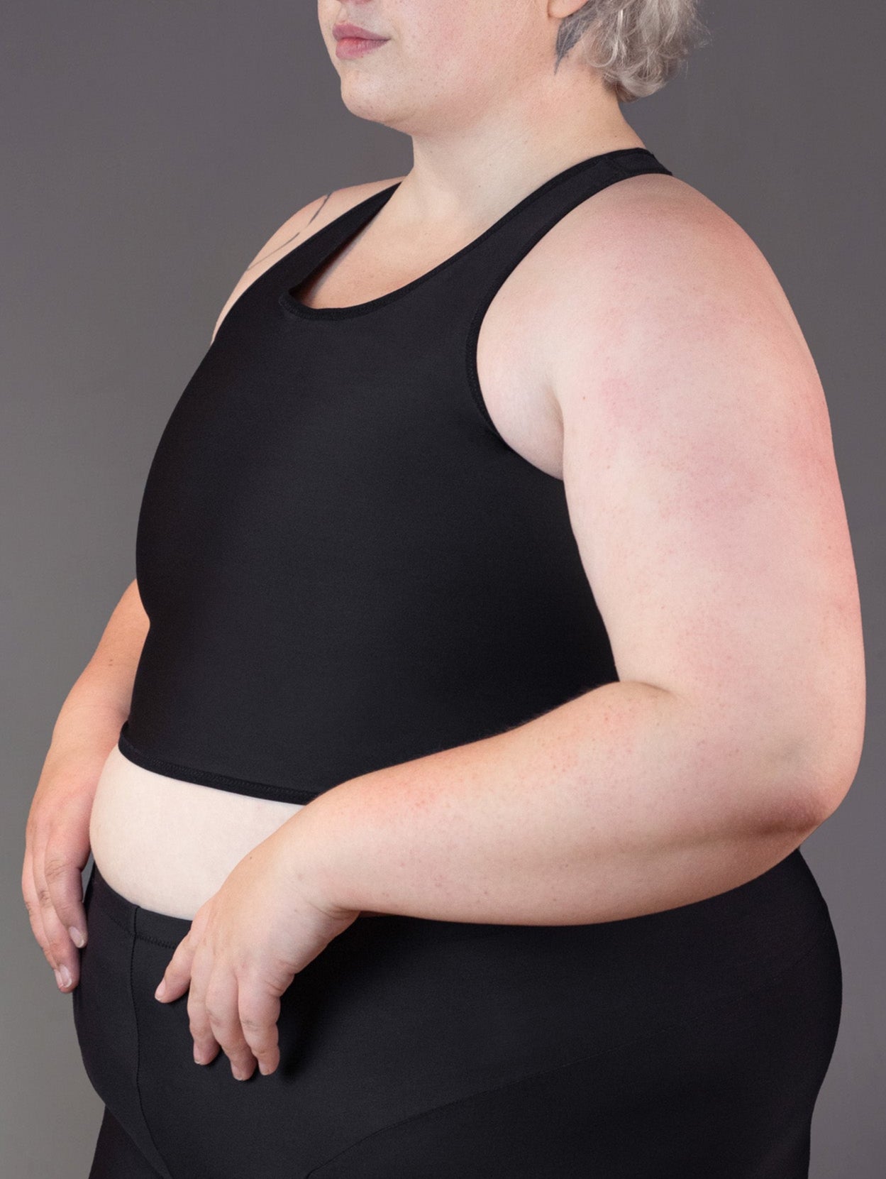 3/4 view of plus size and genderqueer model Jeannette modeling a swim binder in the color black.