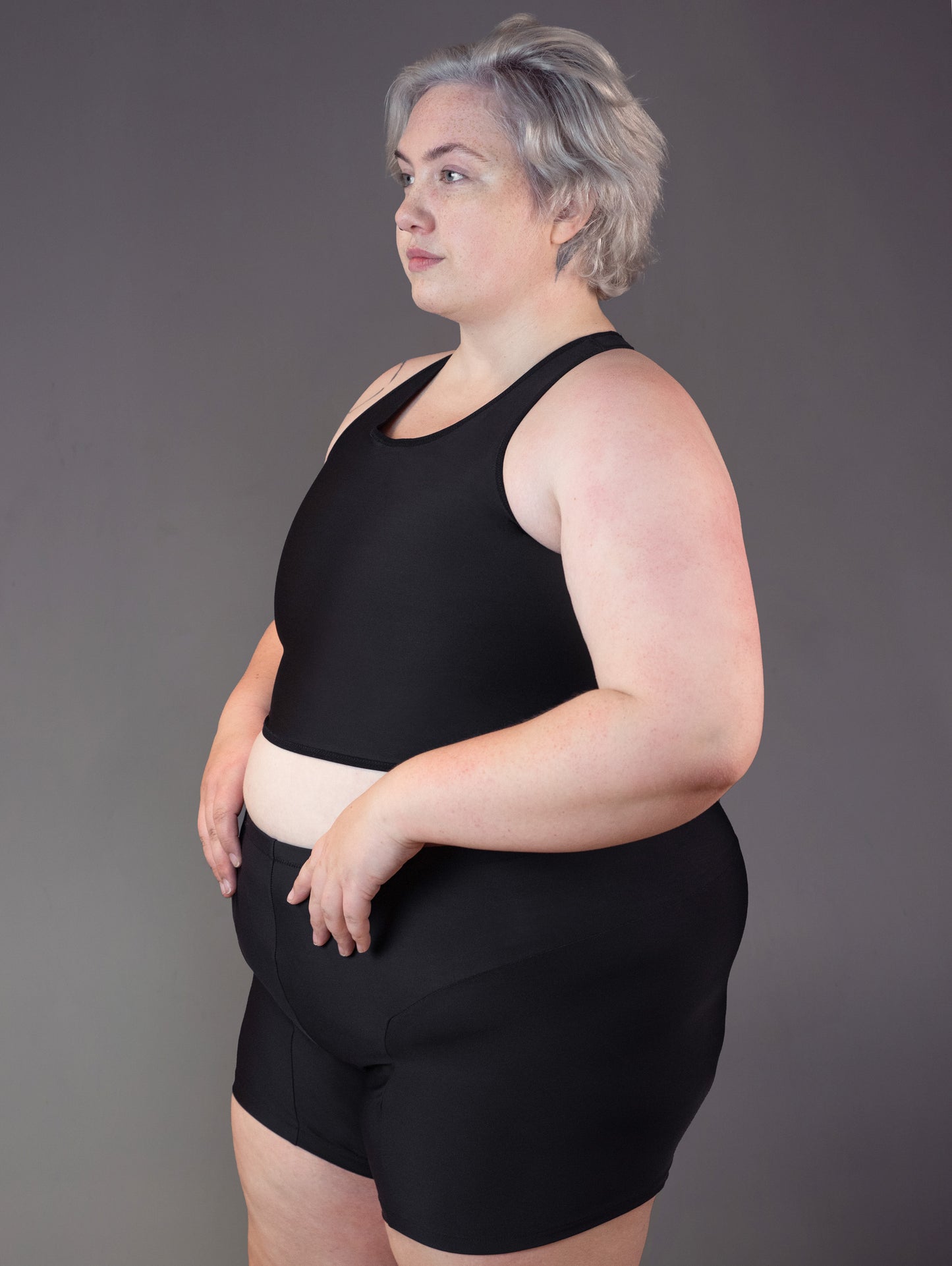 3/4 view of fat and genderqueer model Jeannette modeling a swim binder in the color black.