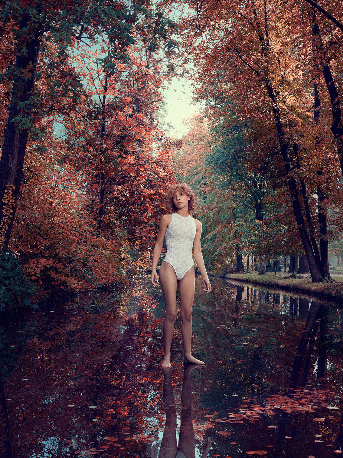 Image of model Lo standing on the water with trees in fall colors in the background